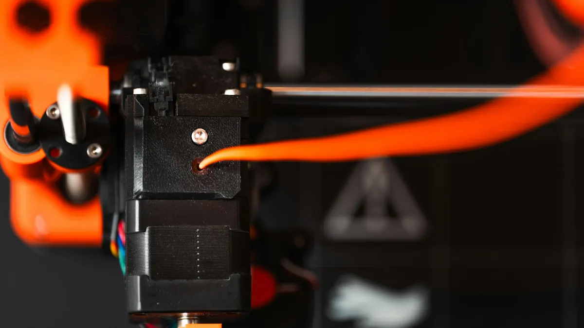 Close-up of an FDM 3D printer extruder feeding orange filament
