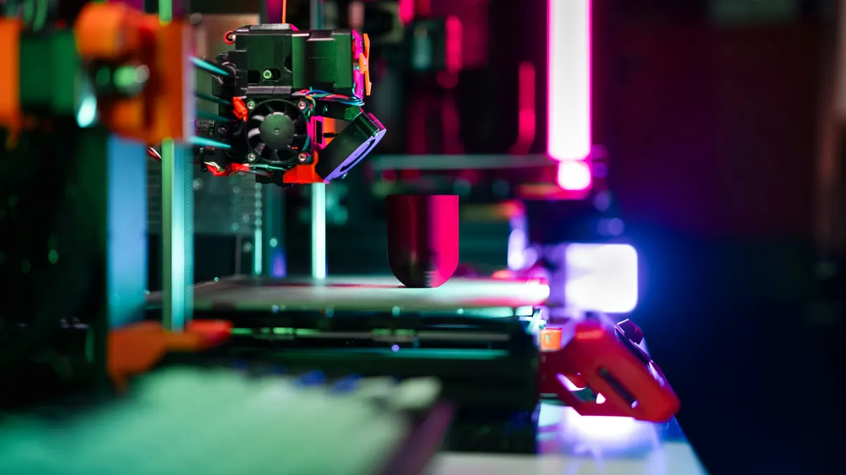 A 3D printer printing a part under coloured workshop lighting