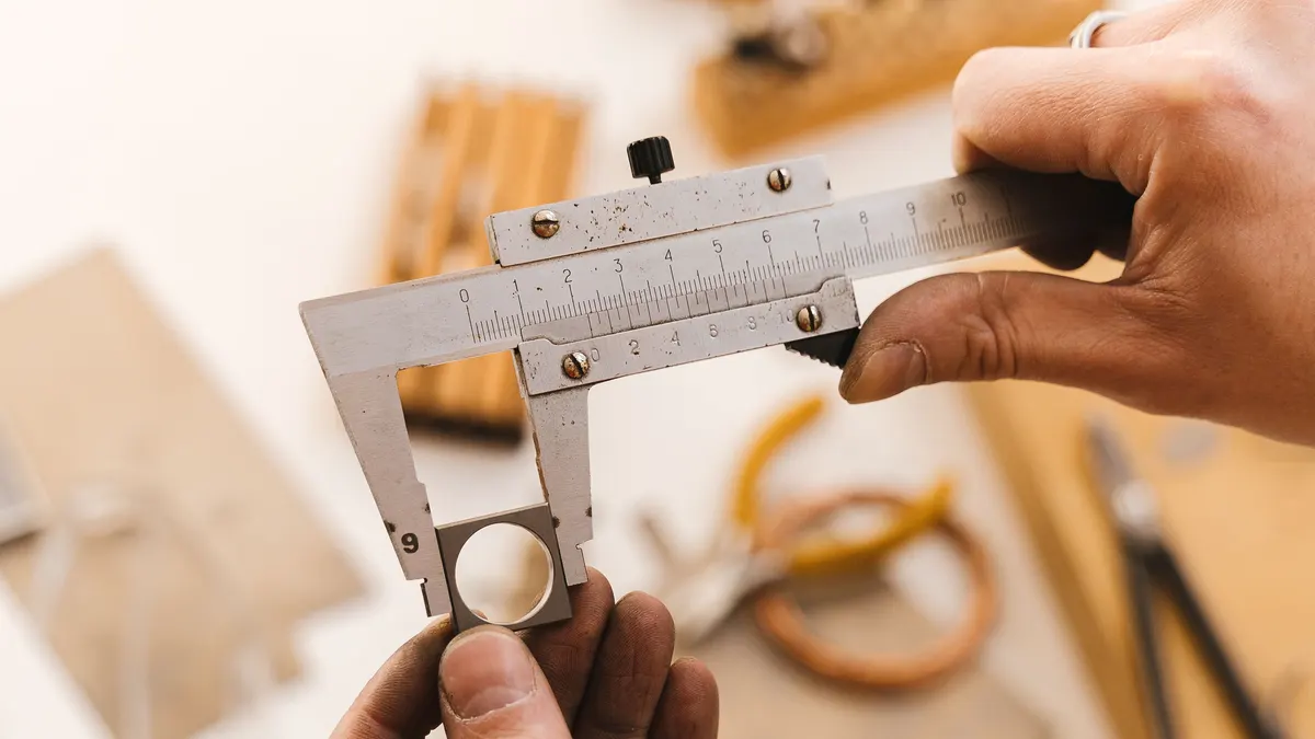 Hands measuring a small part with a vernier caliper